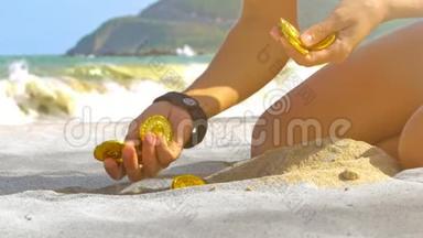 少女手在海洋特写镜头中从沙滩上挑选金币